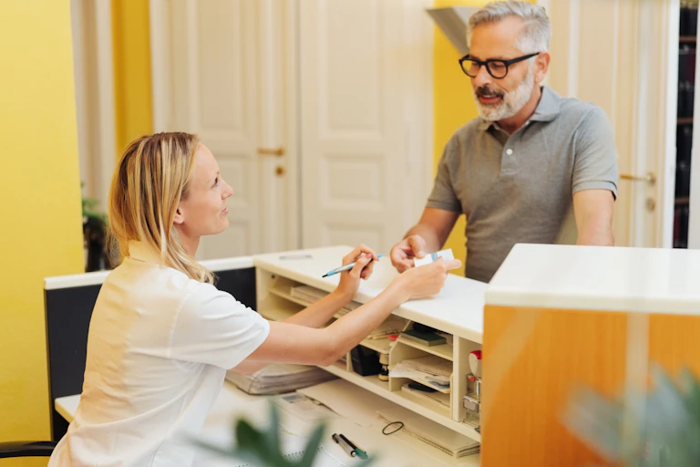 GP practice receptionist hands card to patient