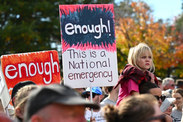 Protest goers, including a small child, at the Canberra rally for women. A sign reads 'enough! This is a national emergency'.