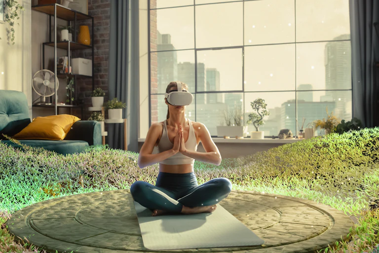 A woman wearing VR goggles places her hands together while sitting on the ground. Virtual greenery surrounds her.