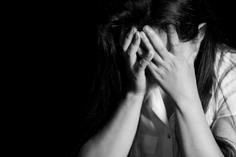 A woman holding her face in her hands against a black backdrop