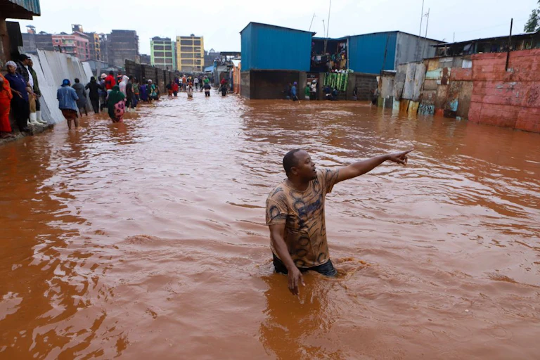 A man wading in the middle of a pool of muddy water and pointing at something, while several other people are seen standing off to the side.