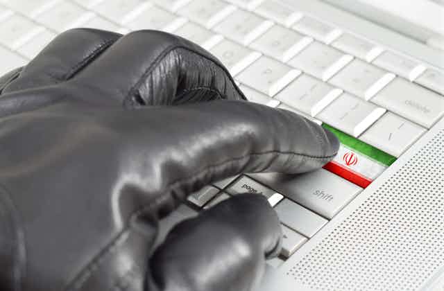 A hand in a glove presses a button on a keyboard decorated with the Iranian flag.