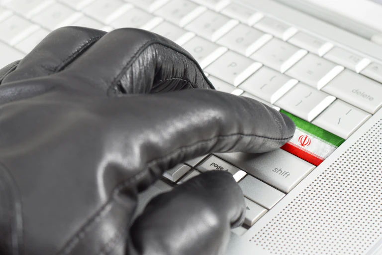 A hand in a glove presses a button on a keyboard decorated with the Iranian flag.
