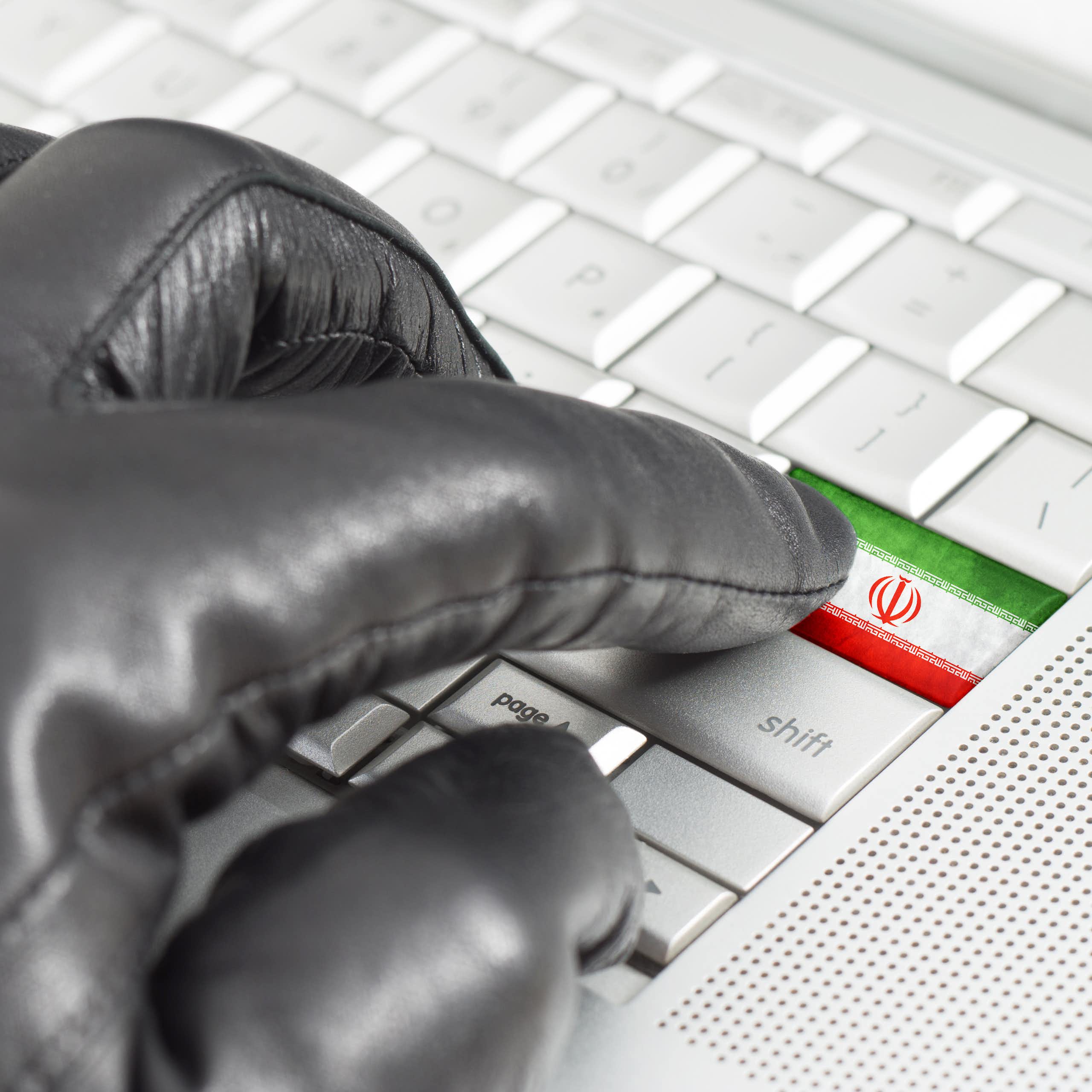 A hand in a glove presses a button on a keyboard decorated with the Iranian flag.