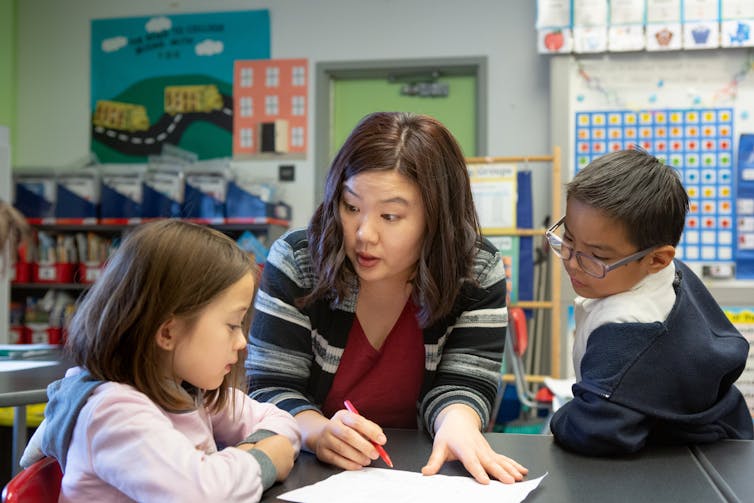 A teacher seen with students at a desk.