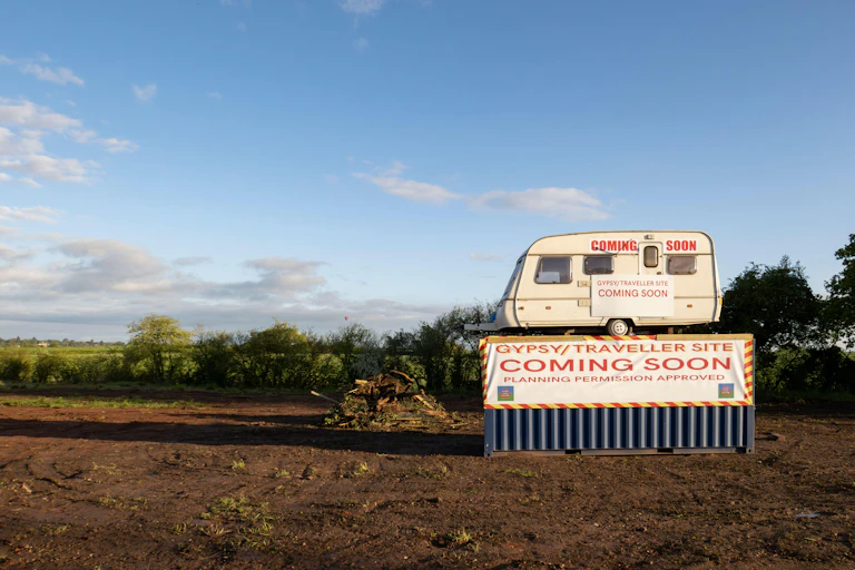 A mobile home sits atop a shipping container in a brown field.