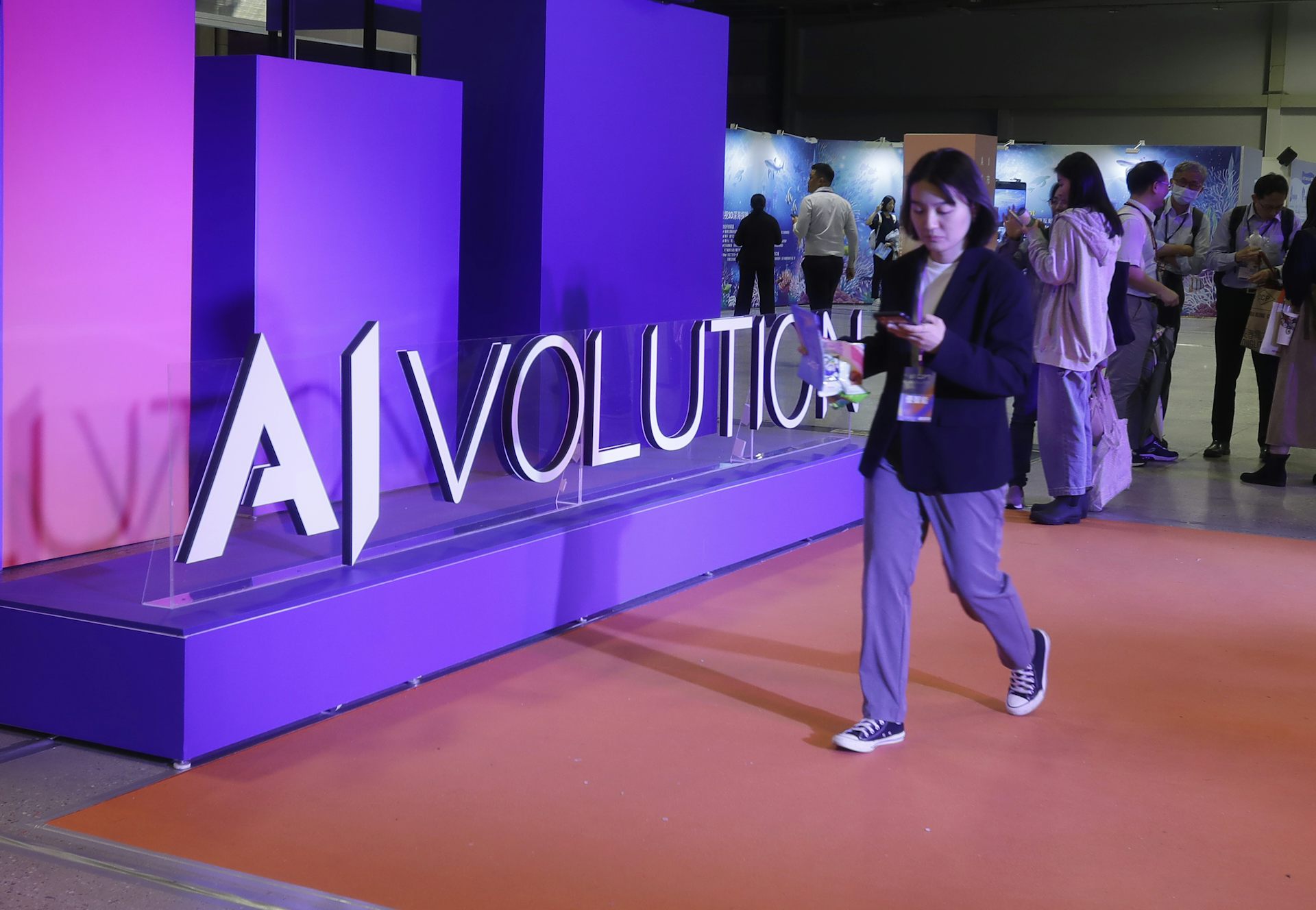 A woman walks past a pink and purple display that reads AIvolution.