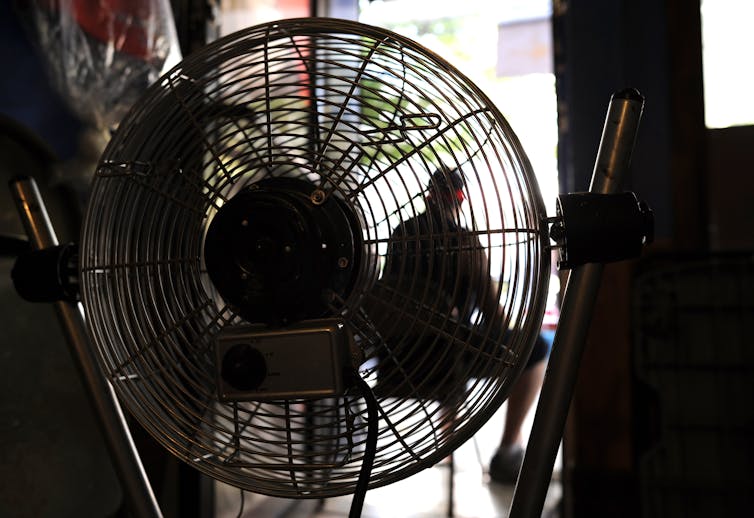 A man sits in the door of a building in Spanish Harlem with a fan running between him and the camera.