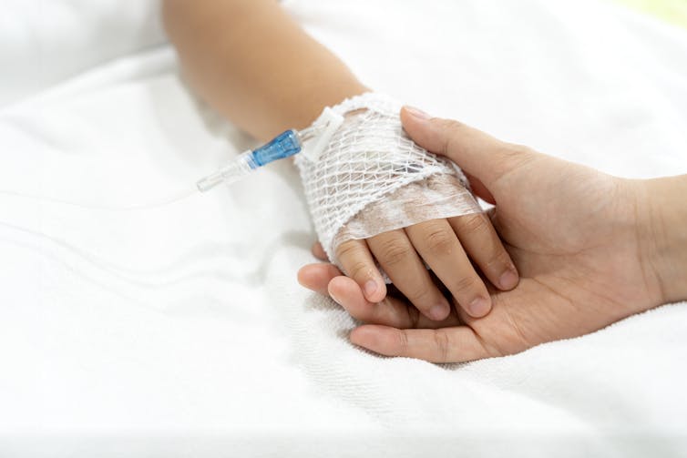 Close-up of a child's hand with an IV tube attached, held by an adult's hand