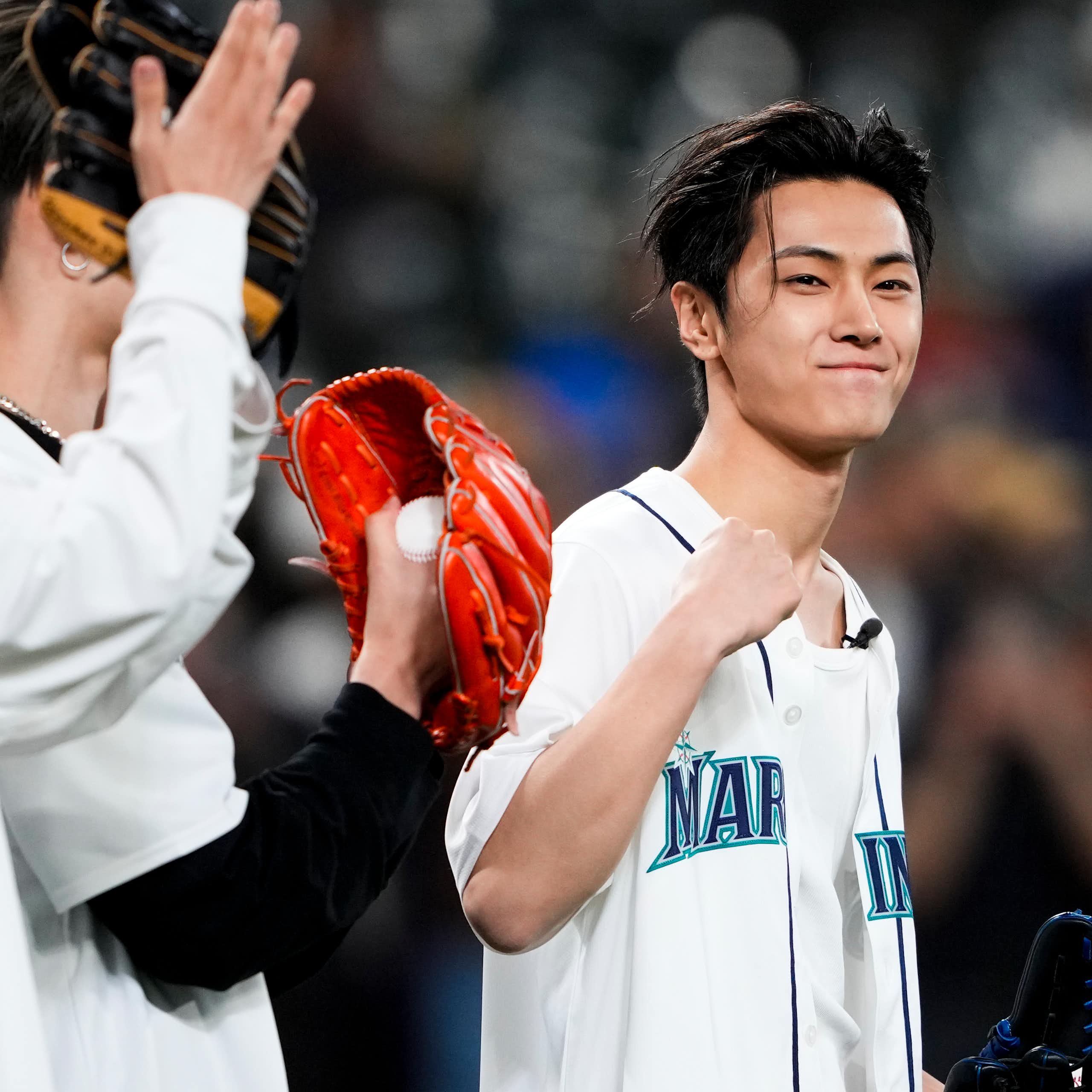 A person seen clenching a victory fist and smiling holding a baseball glove while others look on with gloves. 