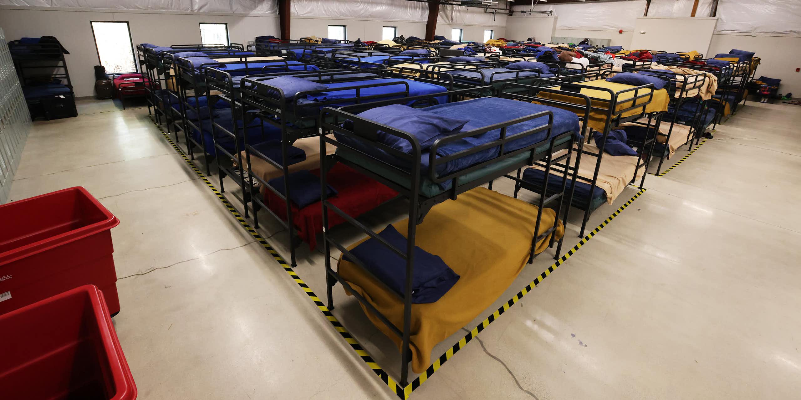 Rows of neatly made bunk beds in a large, brightly lit room.
