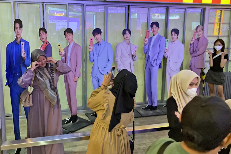 People seen admiring life-sized standup cutouts of a boy band while one person takes a photo.