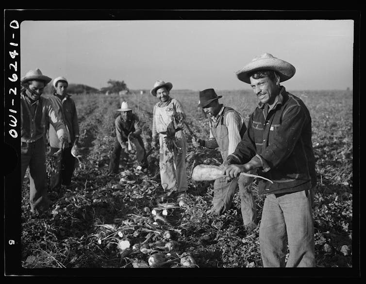 A black and white photo shows men wearing hats standing in a field