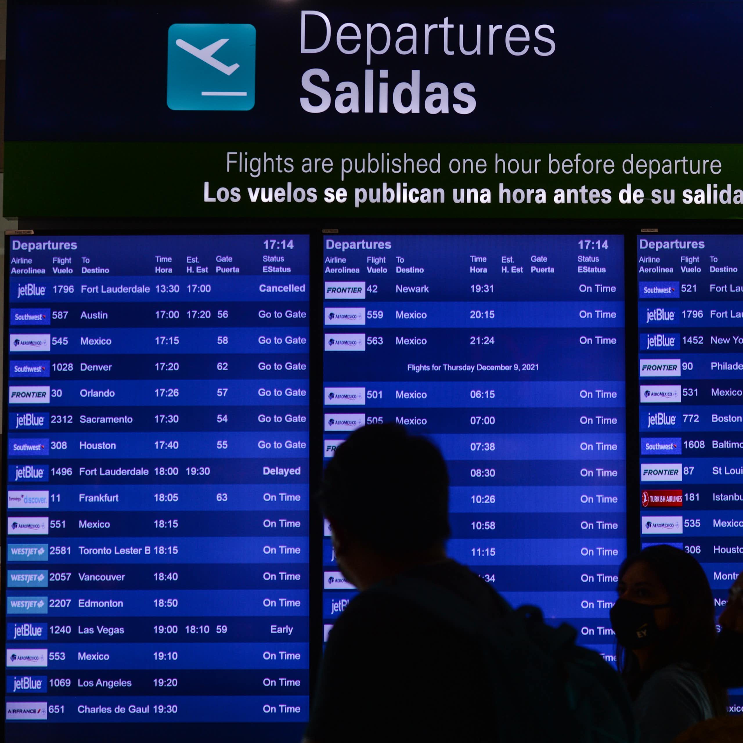 A blue sign displays departures. People are silhouetted in the foreground.