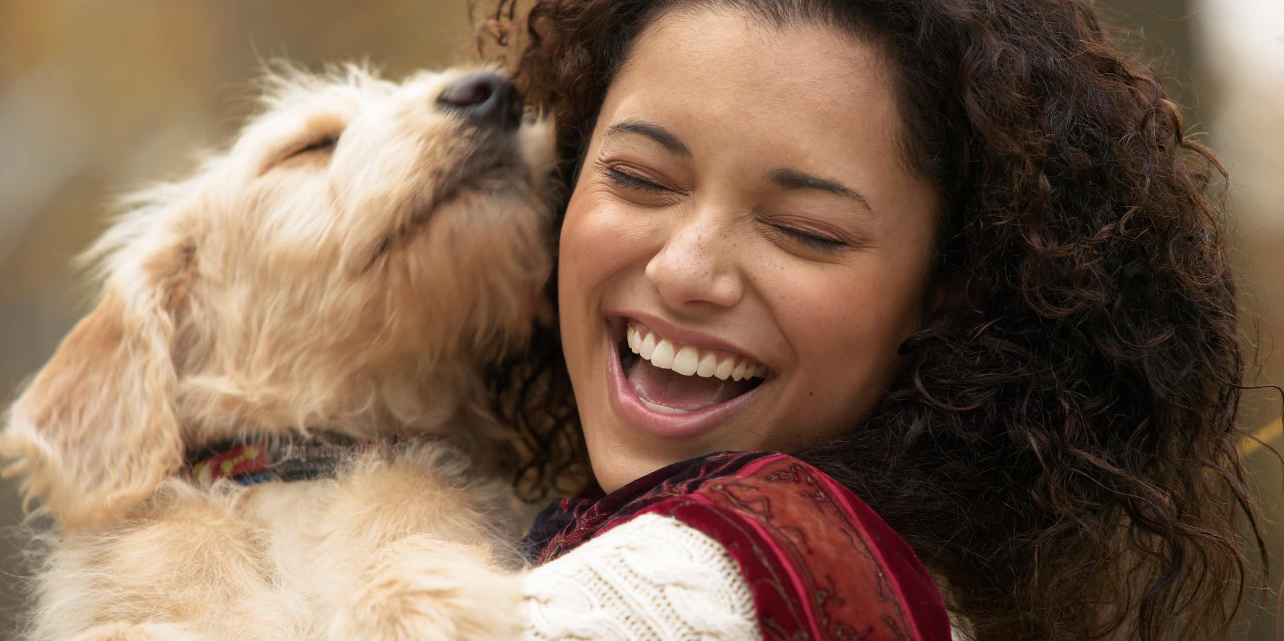 A young woman laughs while holding her dog near to her face.