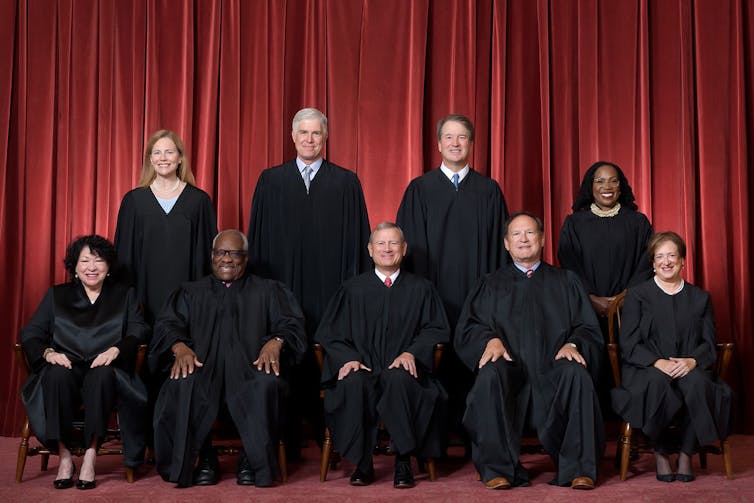 Nine men and women sit in two rows and wear black robes.