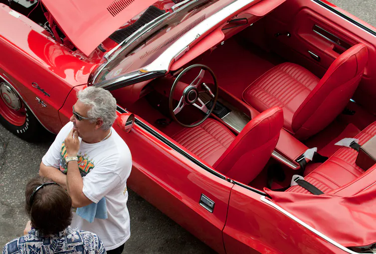 Men stand near a red car.