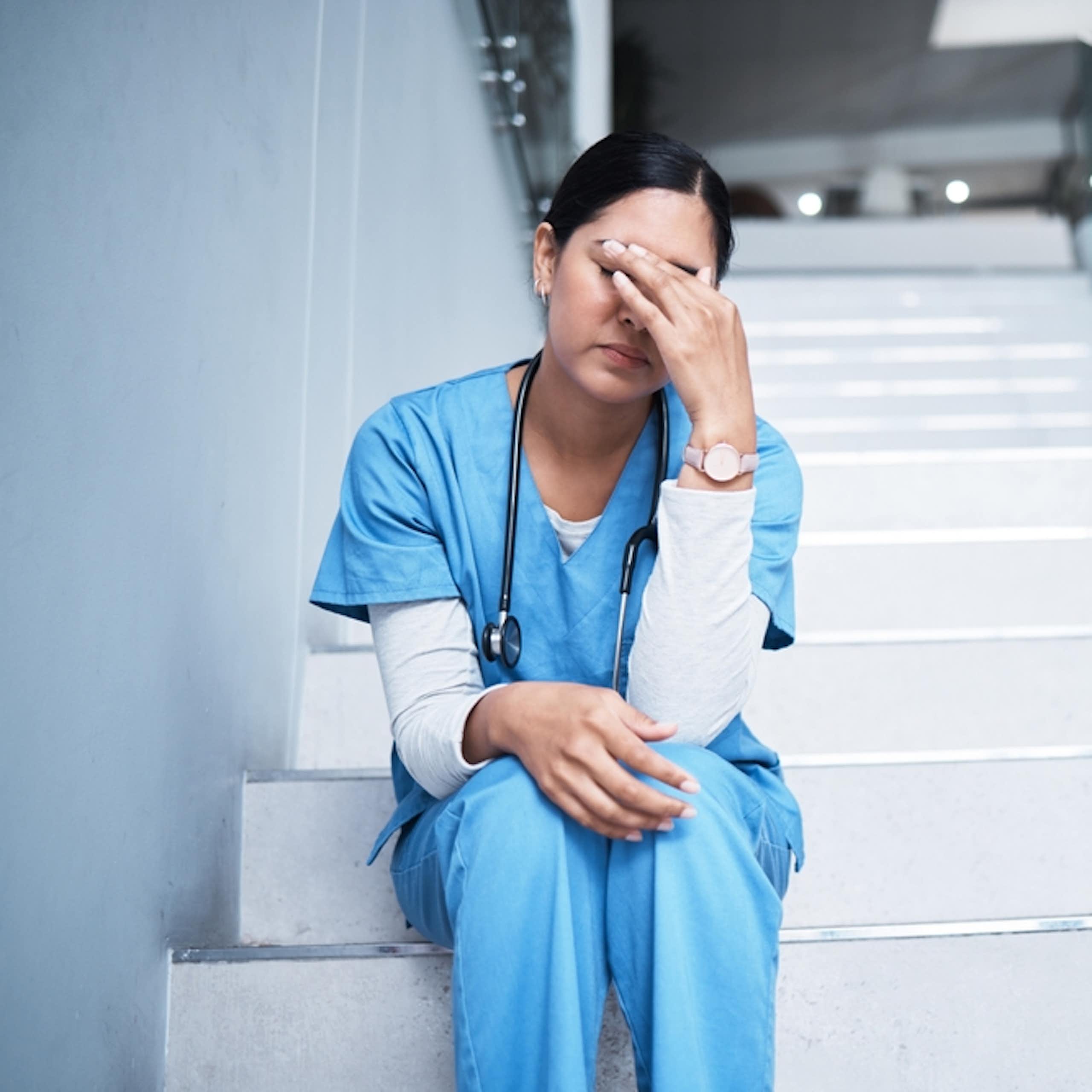 Tired health worker, hand over eyes, sitting on hospital steps