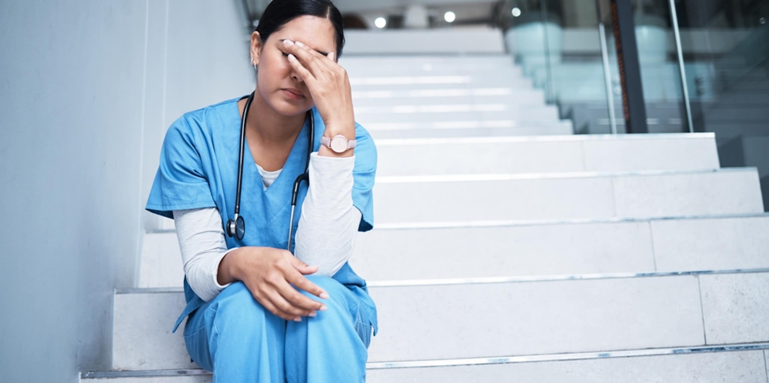 Tired health worker, hand over eyes, sitting on hospital steps