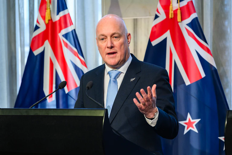 Christopher Luxon at podium with NZ flags