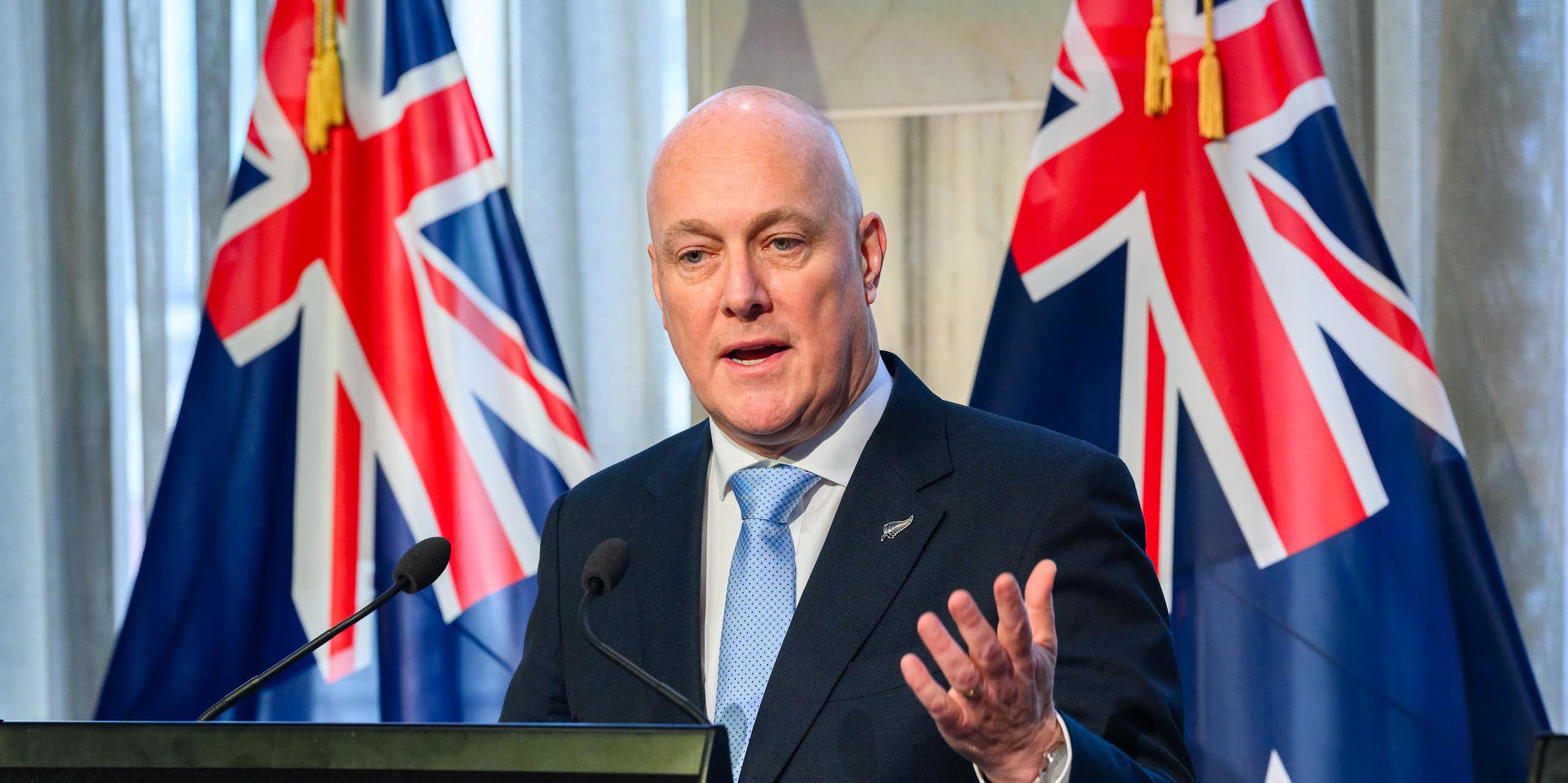 Christopher Luxon at podium with NZ flags