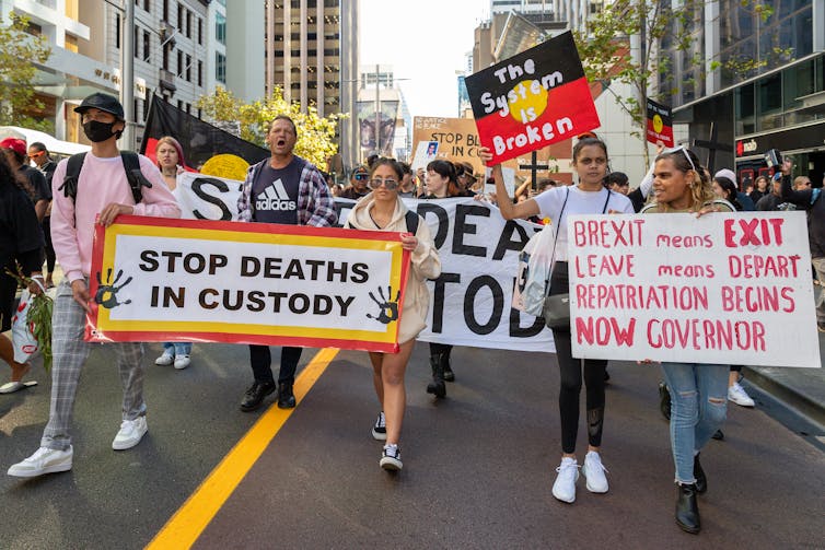 People marching in a protest with signs saying STOP DEATHS IN CUSTODY