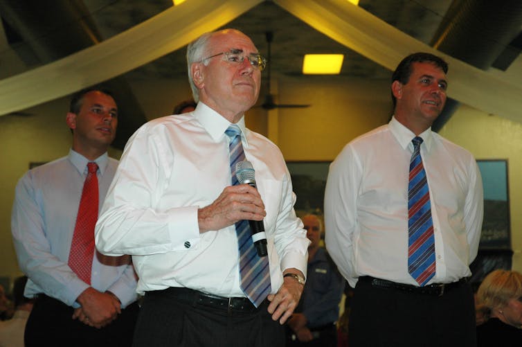 Three men in white shirts and ties stand in a room.