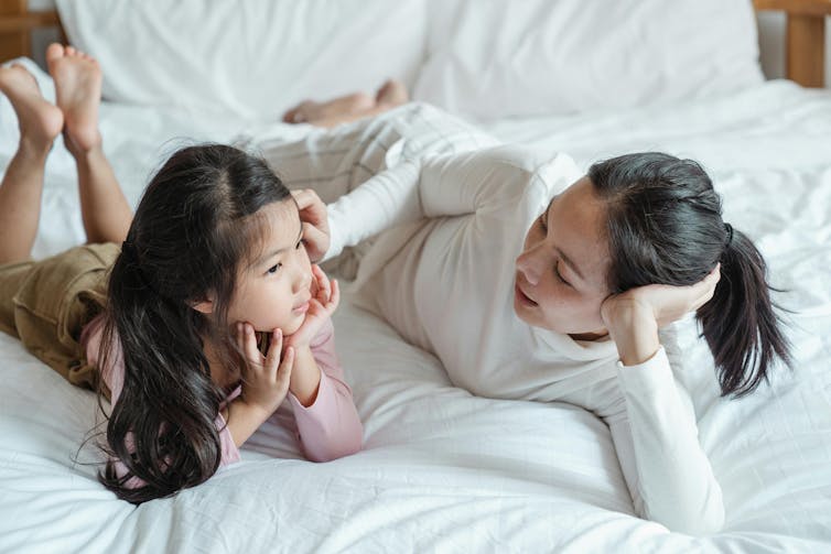 A mother and daughter lie on a bed talking to each other.