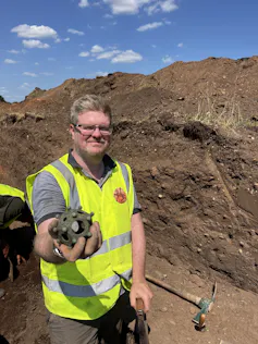 Man holding the dodecahedron at the site of the dig.