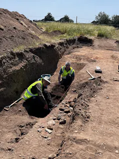Two men digging in a small trench.