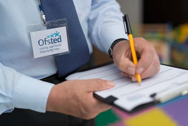 Man with Ofsted lanyard writing on clipboard