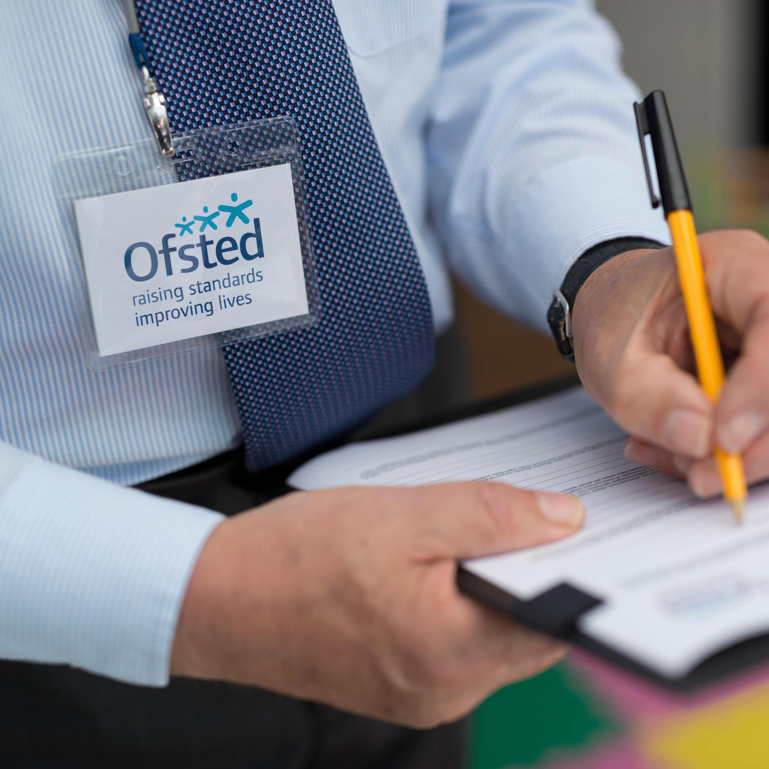 Man with Ofsted lanyard writing on clipboard