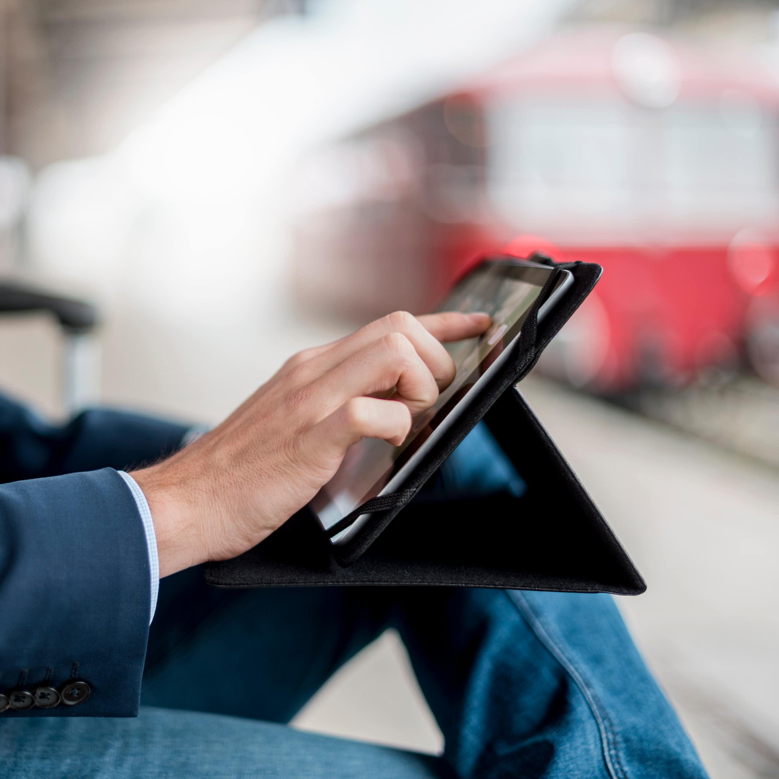 A businessman in a suit is seen using a tablet computer in a train station.