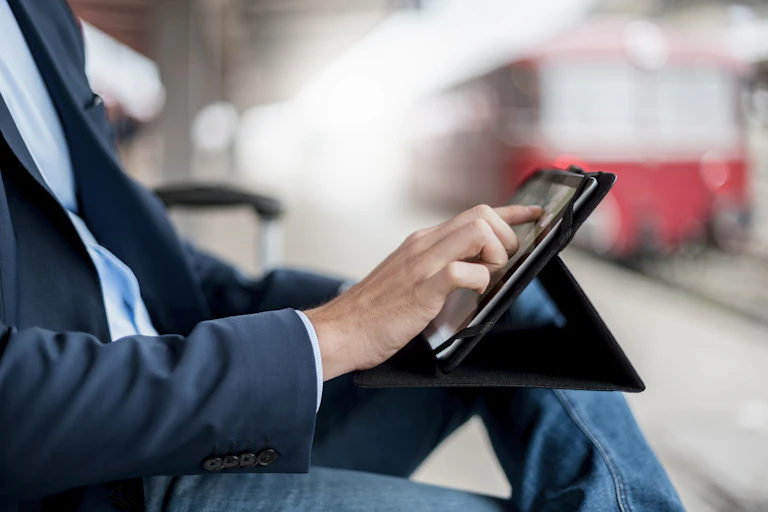 A businessman in a suit is seen using a tablet computer in a train station.