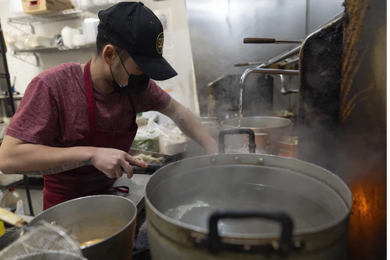 A man stands over a kitchen stove.