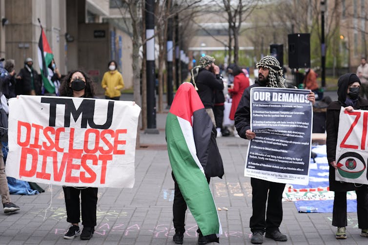 Manifestantes con un cartel de 'TMU disclose divest' y una bandera palestina.