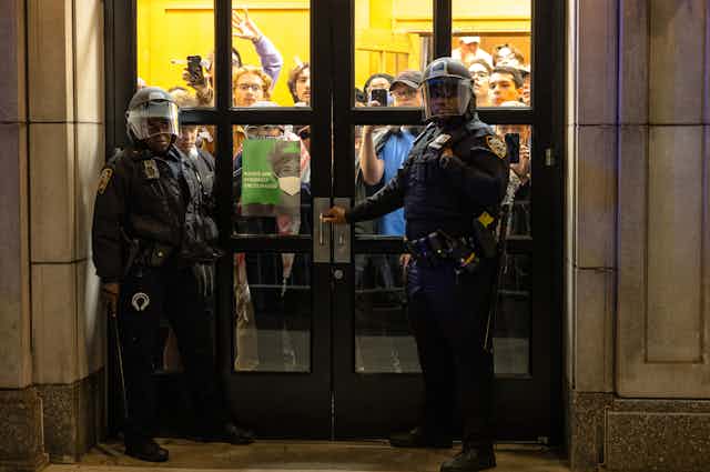 Two police officers stand in front of the doors of a college building that students have taken over.