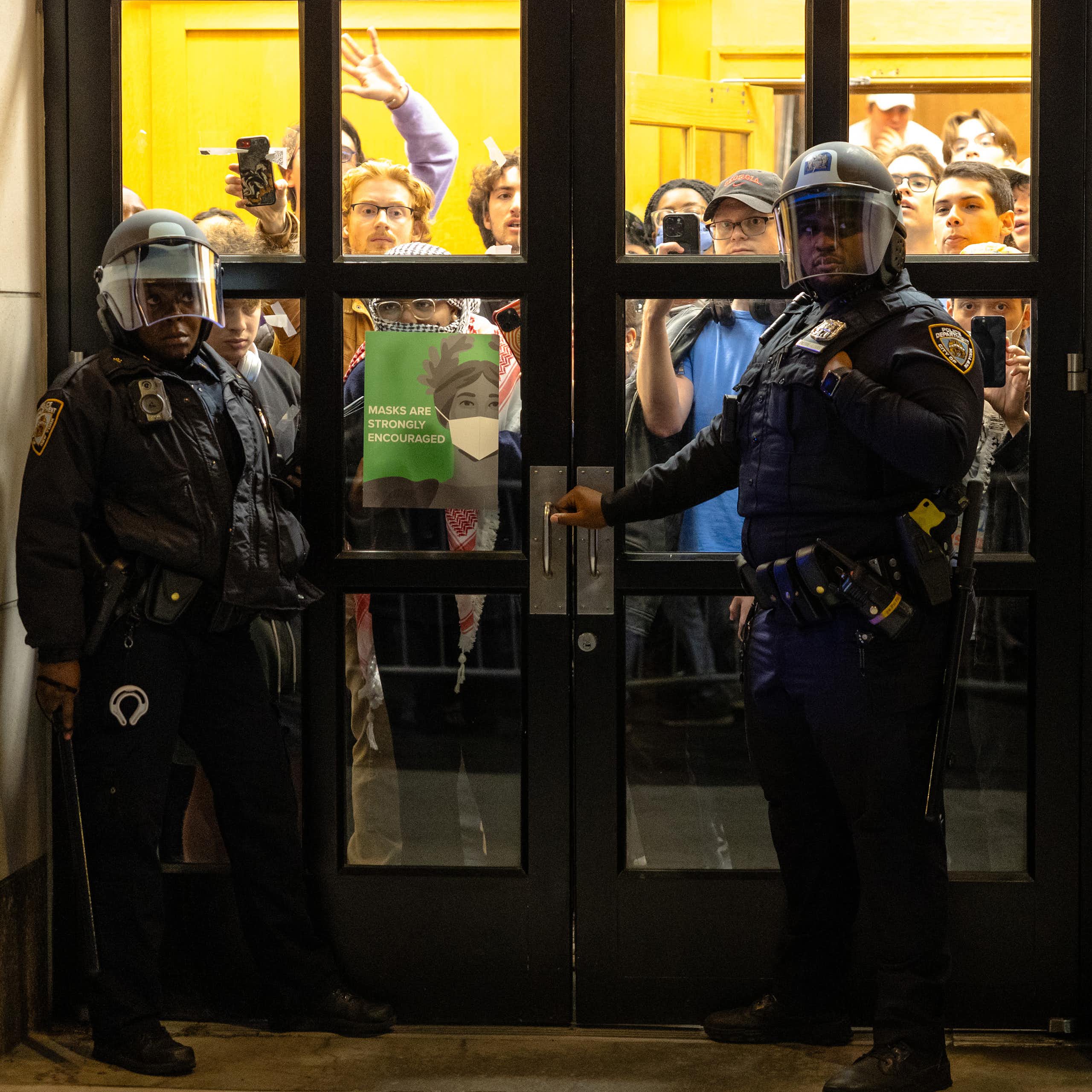 Two police officers stand in front of the doors of a college building that students have taken over.