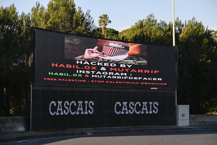 A billboard reads “Hacked” and a pro-Palestinian message.