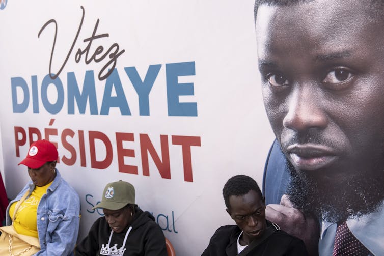 Trois personnes se tiennent devant l’affiche politique du candidat Bassirou Diomaye Faye