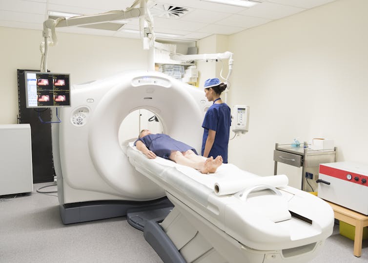 Patient lying in CT machine while radiologist looks on