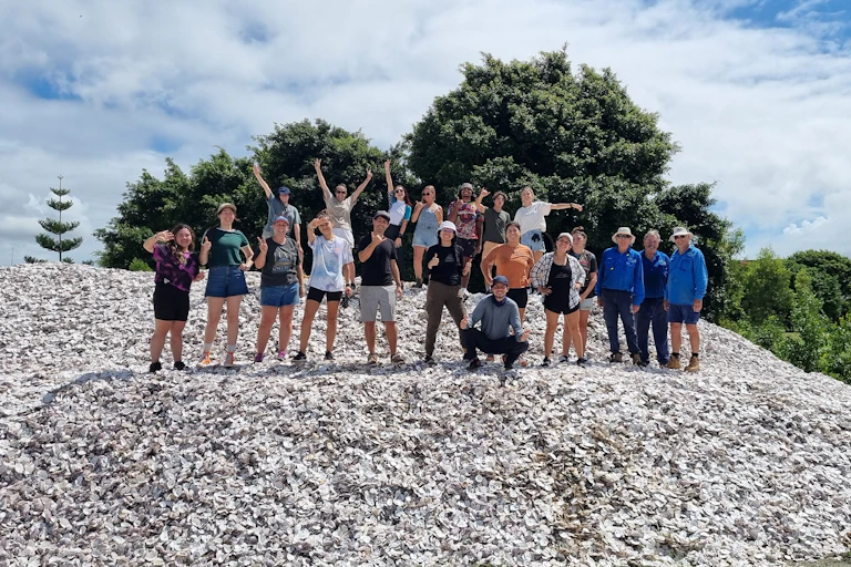 Shell collecting volunteers standing on a huge mound of shell