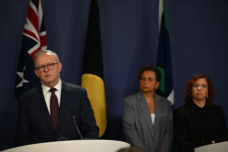 Prime Minister Anthony Albanese at a press conference. He stands in front of a lecture with an Australian flag behind him.