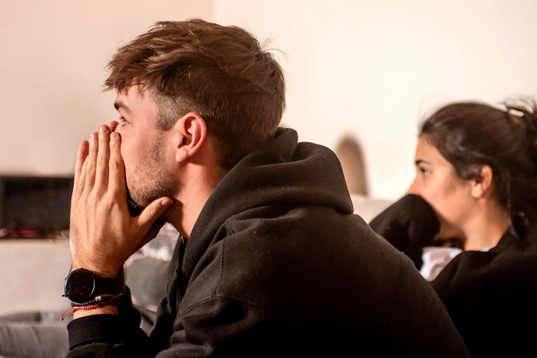 A man and woman tensely watch television