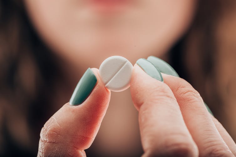 Partial view of woman showing pill in hand.