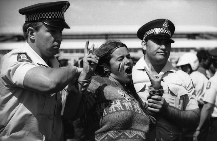 An Aboriginal woman with a police officer on either side of her getting arrested at a protest.