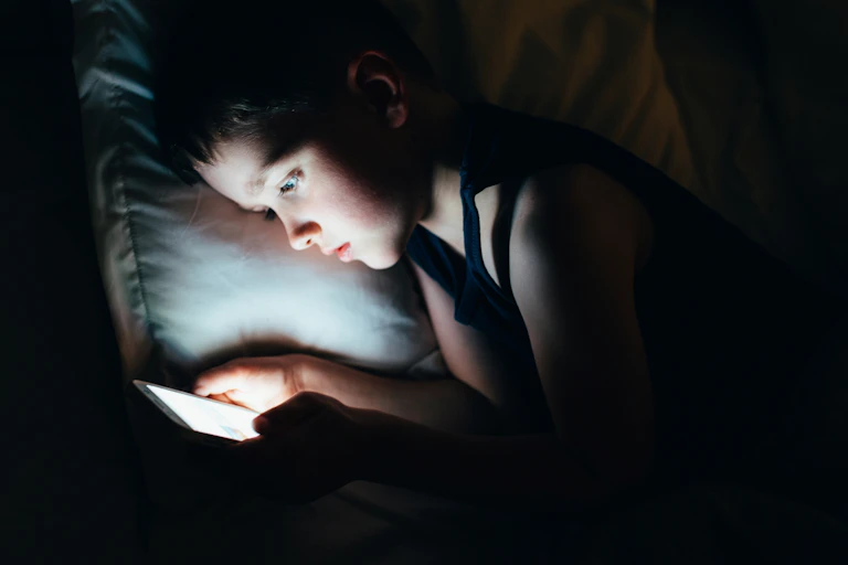 A young boy late at night on a smartphone in bed.