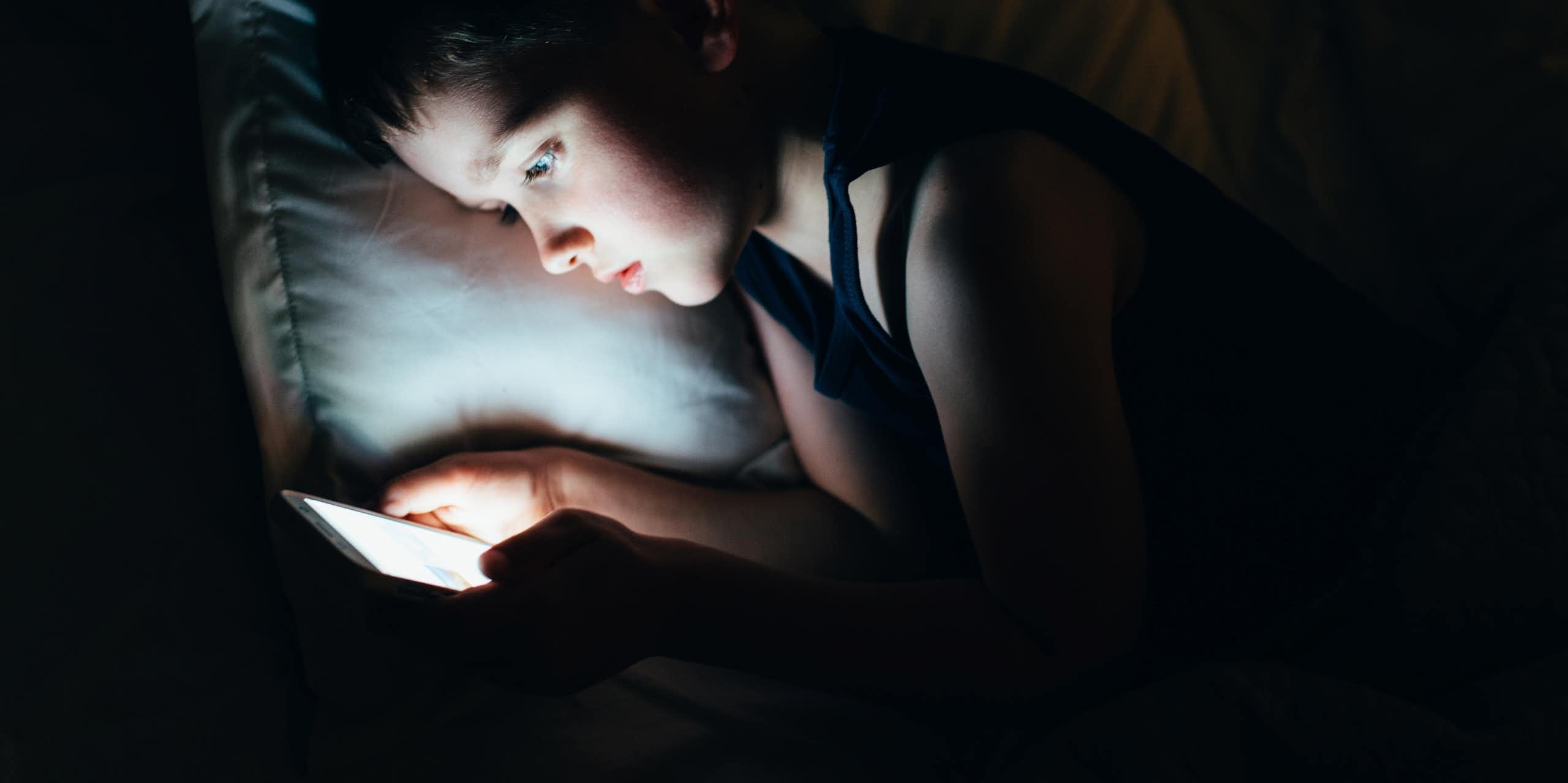 A young boy late at night on a smartphone in bed.