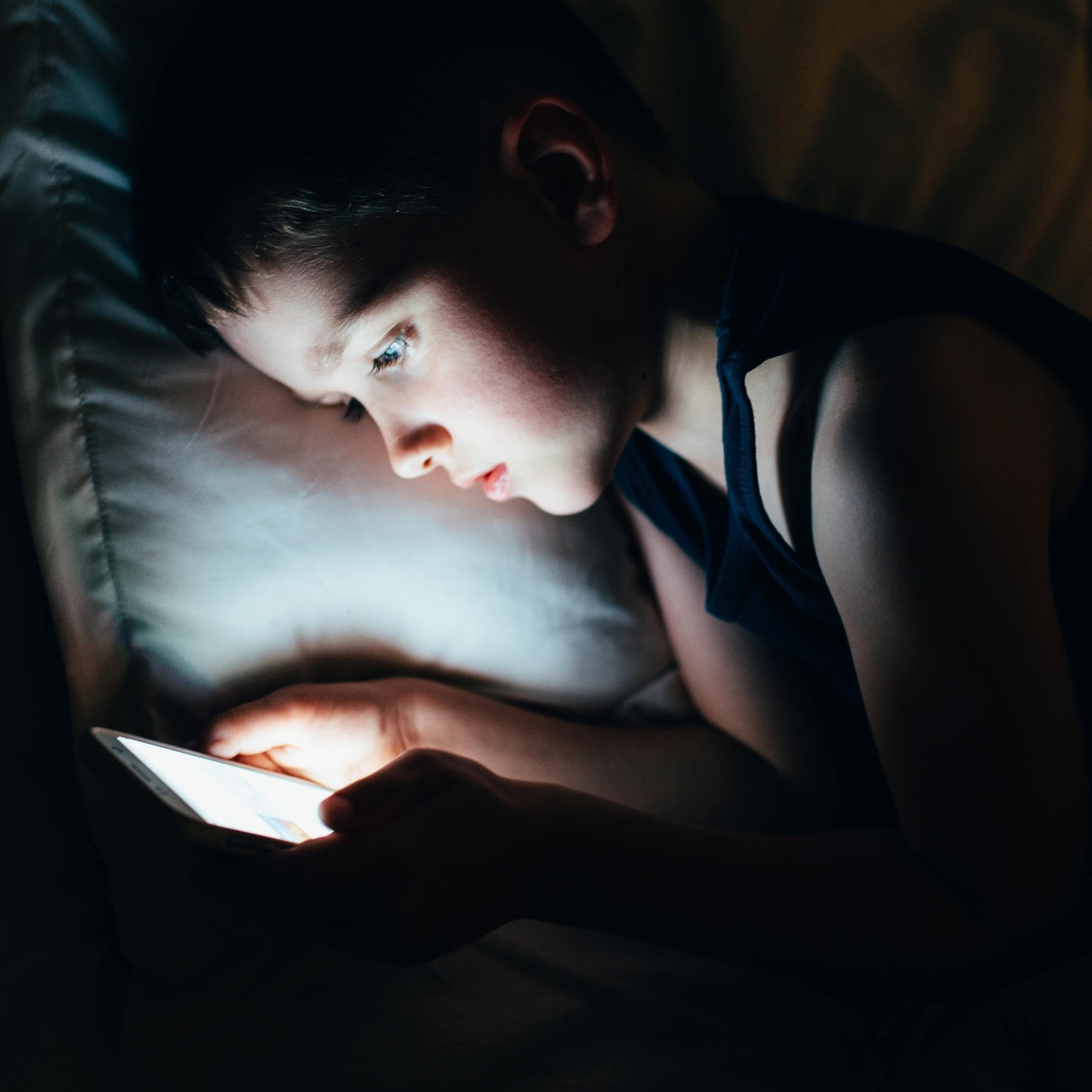 A young boy late at night on a smartphone in bed.