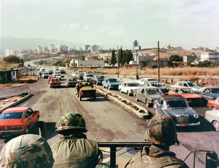 US marines sat on the back of a truck on a busy highway.